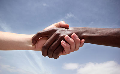 Black hand and white hand shaking with bright blue sky in the background.